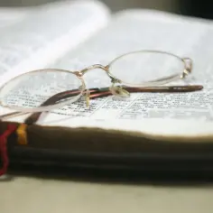Okulary spoczywają na otwartej księdze, symbolizując chwilę refleksji i modlitwy. Wierzę w Boga, a ta księga jest moim przewodnikiem.