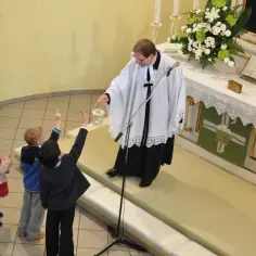 Dzieci na nabożeństwie u luteran. Ksiądz z latarenką, dzieci podnoszą ręce.