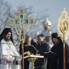 Uroczystość Bożego Narodzenia u prawosławnych. Duchowni w szatach liturgicznych, krzyż, ikona i cerkiew w tle.