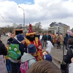 Kolorowy strój postaci z brodą i pióropuszem na głowie przyciąga uwagę dzieci. Tłum ludzi na ulicy, chmury na niebie. Krakowskie odpusty wielkanocne to zawsze barwne wydarzenia.