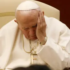 Papież Jan Paweł II w białej szacie, z ręką na skroni, siedzi na krześle.