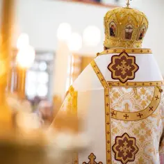 Biskup w bogato zdobionej szacie i mitrze podczas nabożeństwa grekokatolickiego. W tle płoną świece.
