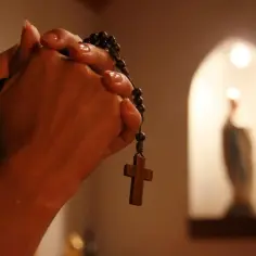 Dłonie trzymające różaniec, z krzyżem zwisającym w dół. W tle, w niszy, widać postać Matki Boskiej. To może być 7 października, dzień modlitwy.
