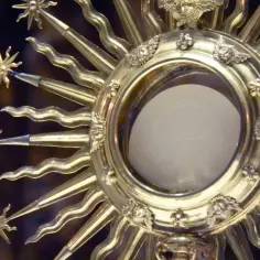 Złota monstrancja ze Słońcem, symbolizująca obecność Chrystusa, jest sercem adoracji. W jej centrum biały opłatek z krzyżem.