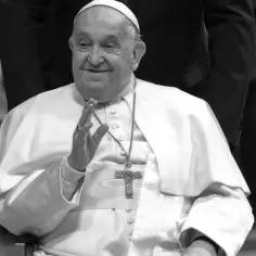 Papież Franciszek, w białej sutannie i z krzyżem, pozdrawia. Jego życiorys to historia pokory i służby.