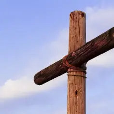 Drewniany krzyż, symbol cierpienia i stygmaty, na tle błękitnego nieba z chmurami.