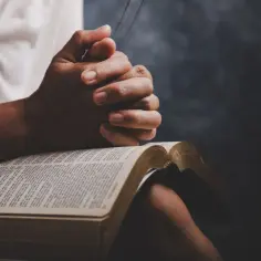 Dłonie złożone do modlitwy nad otwartą Biblią. Odmawiany jest cały pacierz po kolei, szukając pocieszenia i siły w słowach Pisma Świętego.