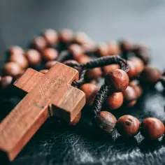Drewniany krzyż i paciorki różańca na ciemnym tle.