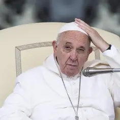 Papież Franciszek w białej szacie siedzi na krześle, dotykając czoła.