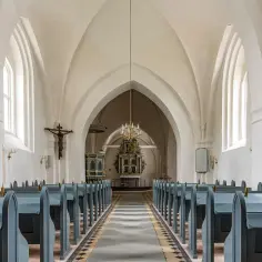 Wnętrze kościoła luterańskiego z ławkami, ołtarzem i krzyżem.