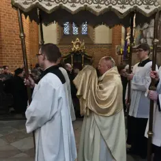 Uroczysta procesja w kościele. Czy to już rezurekcja o której godzinie? Ludzie klęczą na ławkach, duchowni niosą baldachim.