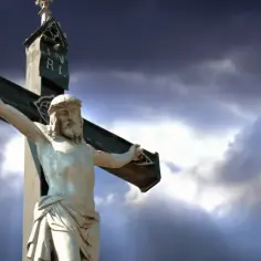 Kamienna figura Jezusa na krzyżu, symbolizująca grób Jezusa, na tle burzowego nieba.