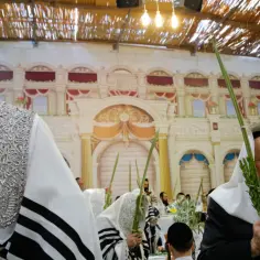 Mężczyźni w tradycyjnych strojach świętują Sukkot, trzymając gałązki i cytrynę. Obchody święta namiotów w synagodze.