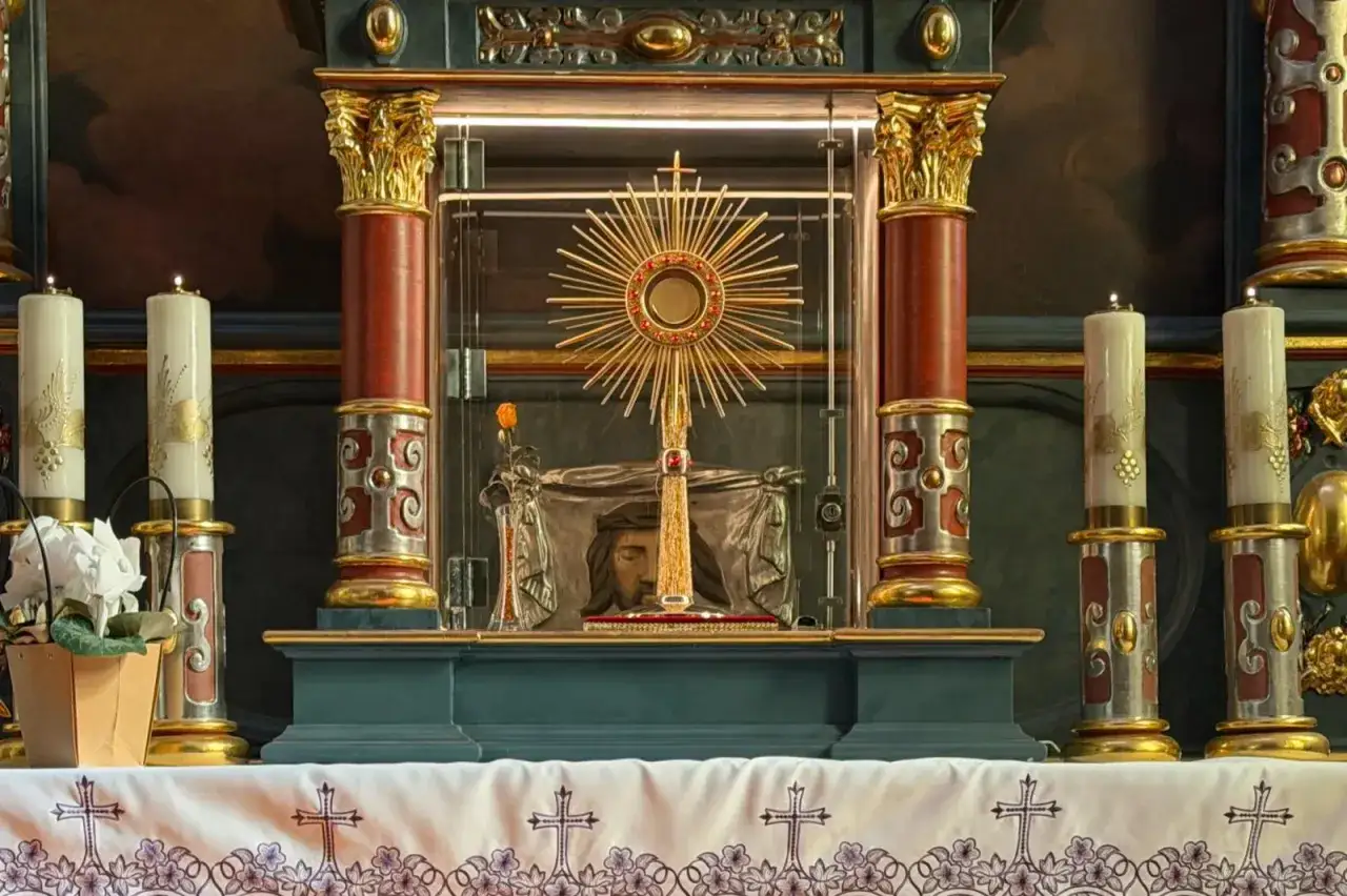 Ołtarz z monstrancją, symbolem adoracji. Wokół świece i ozdobne kolumny.