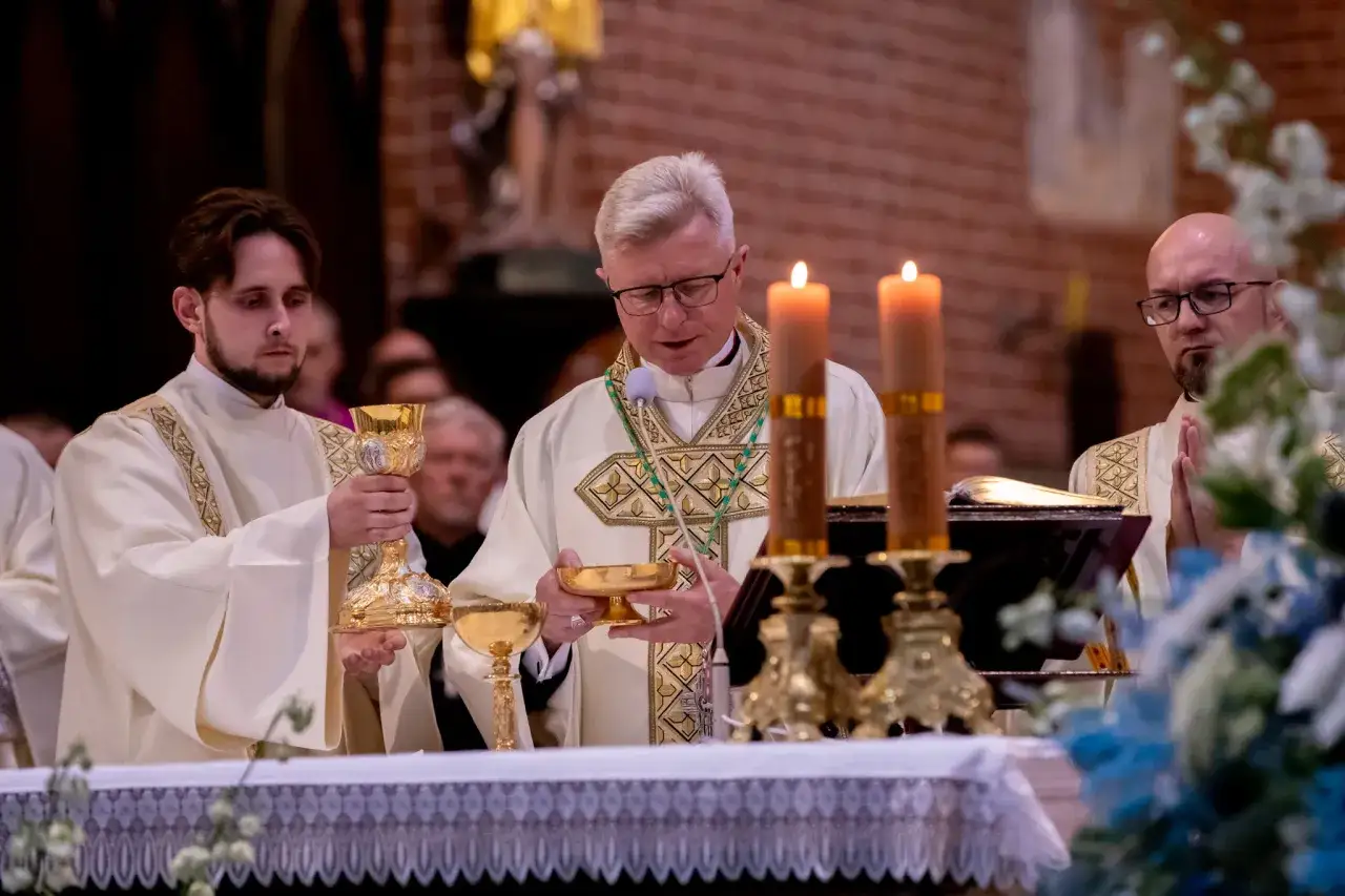 Trzech księży w szatach liturgicznych podczas modlitwy dziękczynnej. Jeden z nich trzyma kielich, inny patrzy w książkę, a trzeci ma złożone ręce.