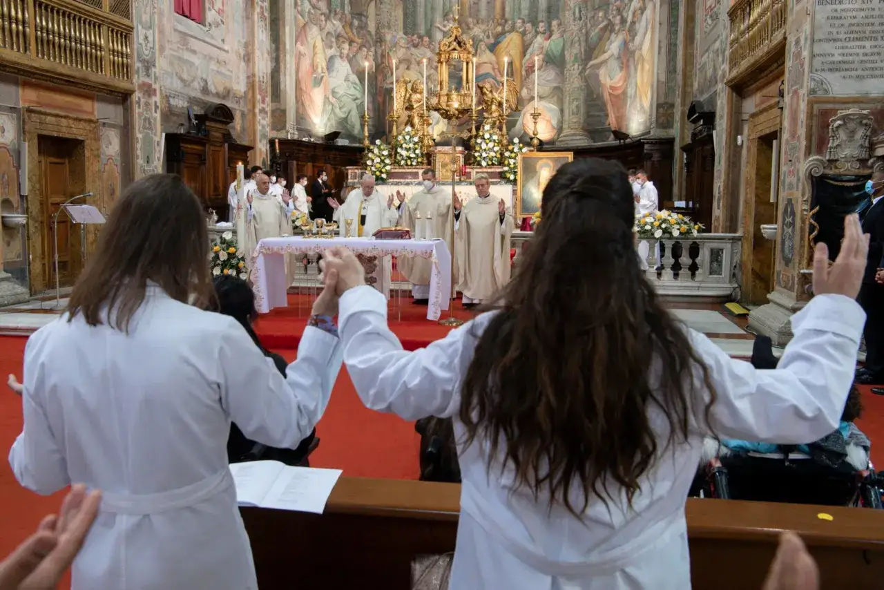 W kościele trwa msza. Dwie osoby w białych szatach trzymają się za ręce, modląc się. Kapłani przy ołtarzu celebrują Eucharystię, symbolizującą ciało Chrystusa.